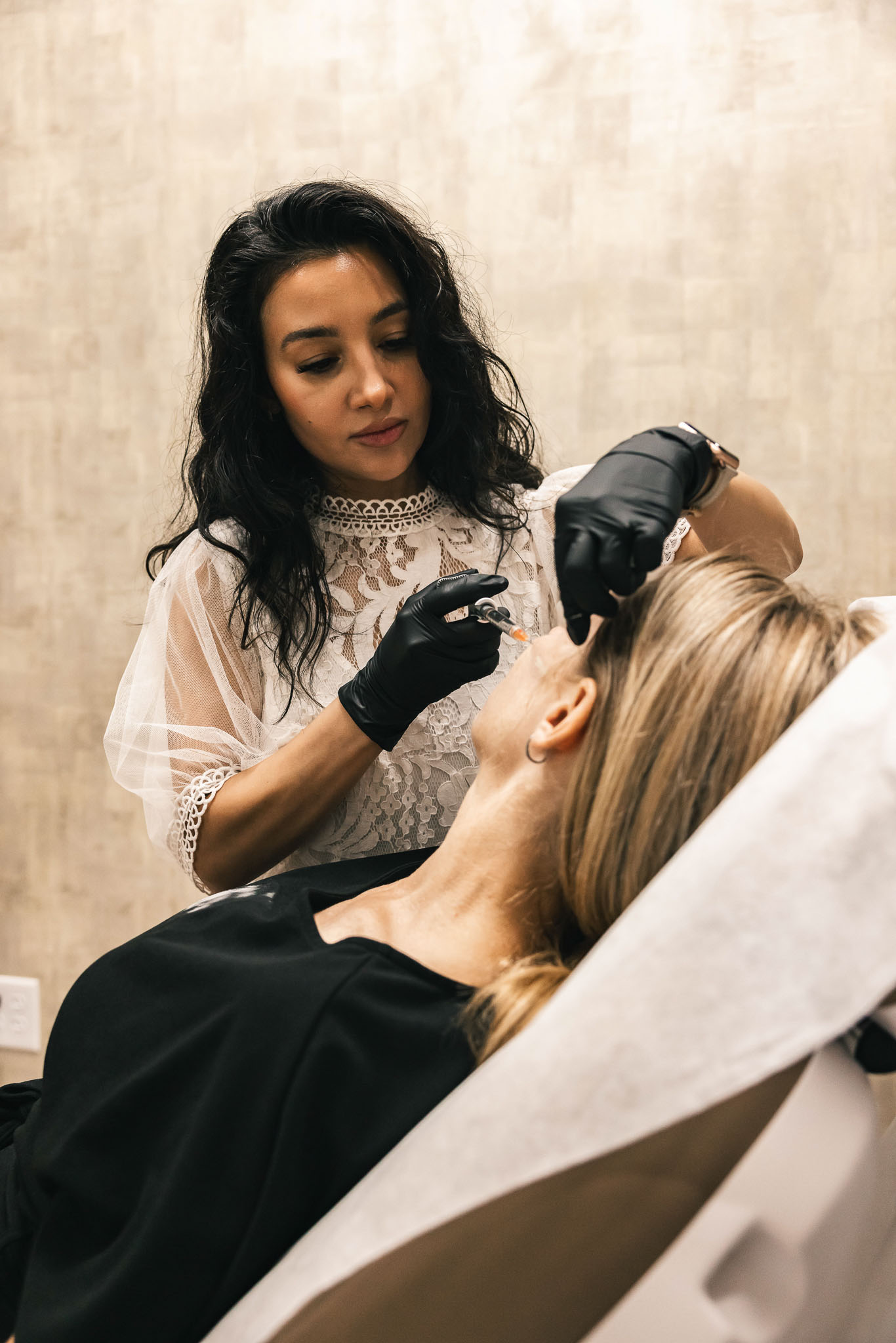 Professional aesthetician wearing black gloves preparing for facial treatment procedure in Mesa, AZ. 