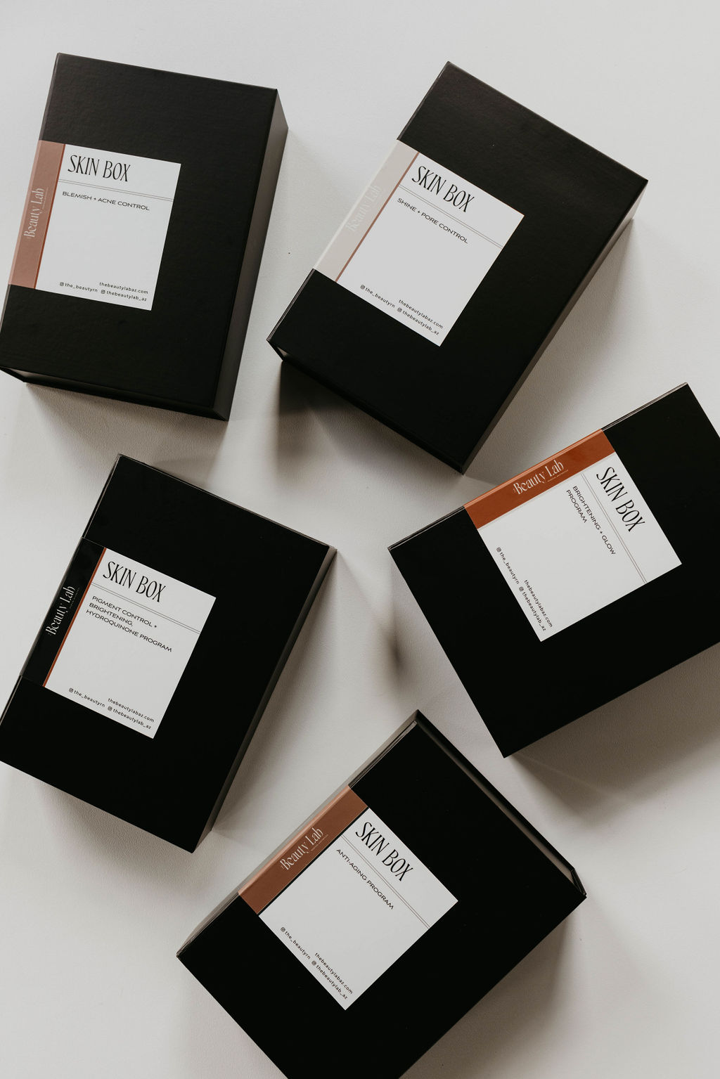 Several black cosmetic or skincare product boxes, called Skin Box, arranged artfully on a light background.